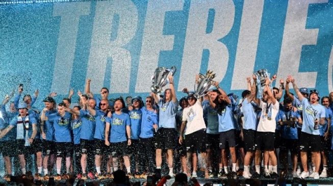 Para pemain Manchester City merayakan di atas panggung dengan trofi mereka setelah parade kemenangan bus atap terbuka untuk kemenangan Piala Eropa, Piala FA, dan Liga Premier mereka, di Manchester, Inggris utara pada 12 Juni 2023. Oli SCARFF/AFP