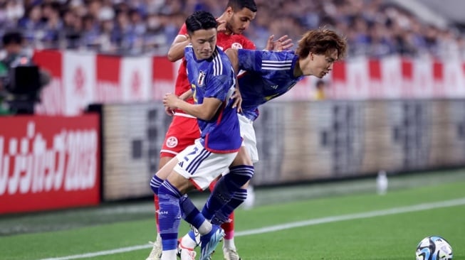 Ko Itakura (kanan) dan Yukinari Sugawara (kiri) dari Jepang berebut bola dengan Elies Ashley dari Tunisia selama pertandingan persahabatan internasional antara Jepang vs Tunisia di Stadion Noevir di Kobe pada 17 Oktober 2023.PAUL MILLER / AFP.